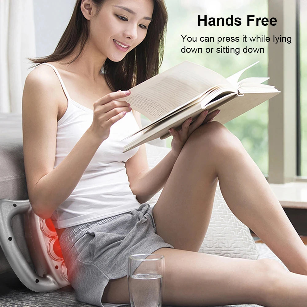 Woman reading a book while using the fascia massage gun on her back , sitting on a couch.