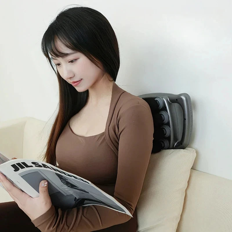 Woman sitting on a couch reading a magazine with a fascia massage gun behind her back.
